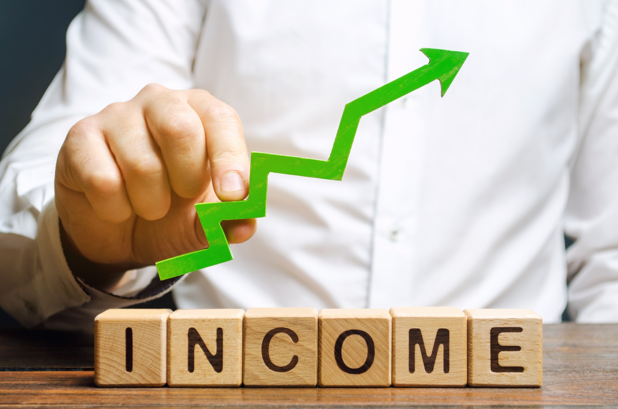 Wooden blocks with the word Income and the up arrow in the hands of businessmen